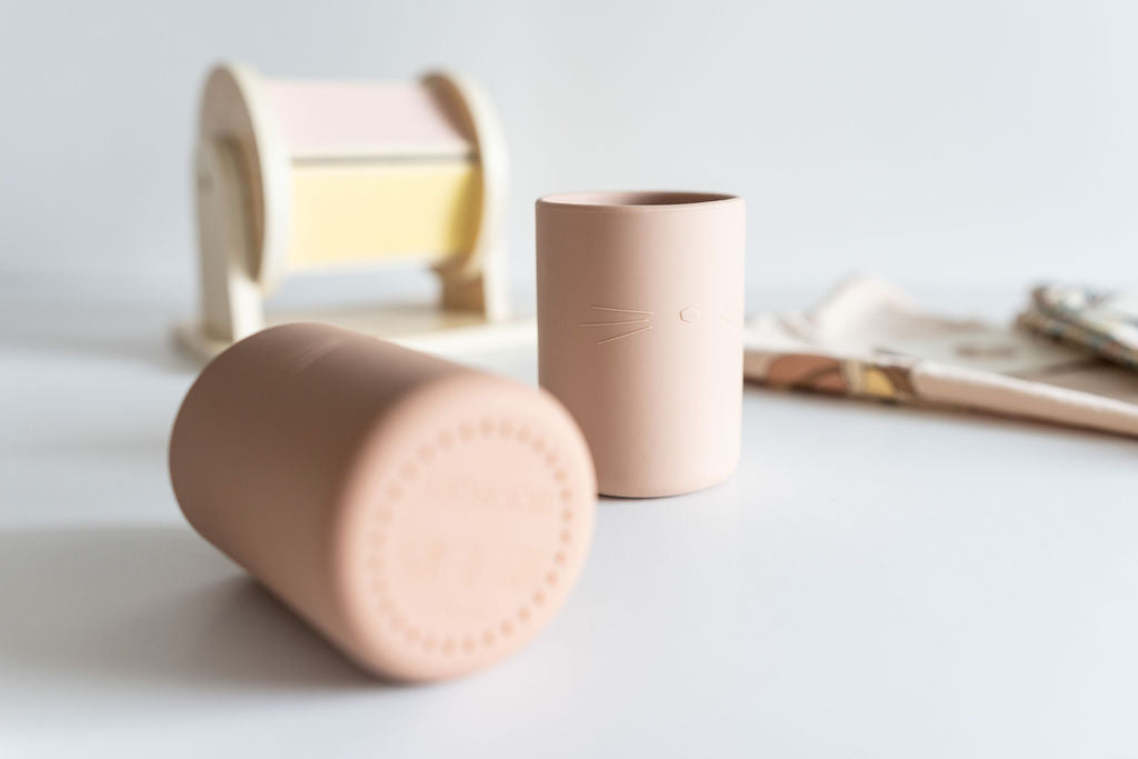 Two cylindrical childrens drinking cups on a light surface with a blurred background