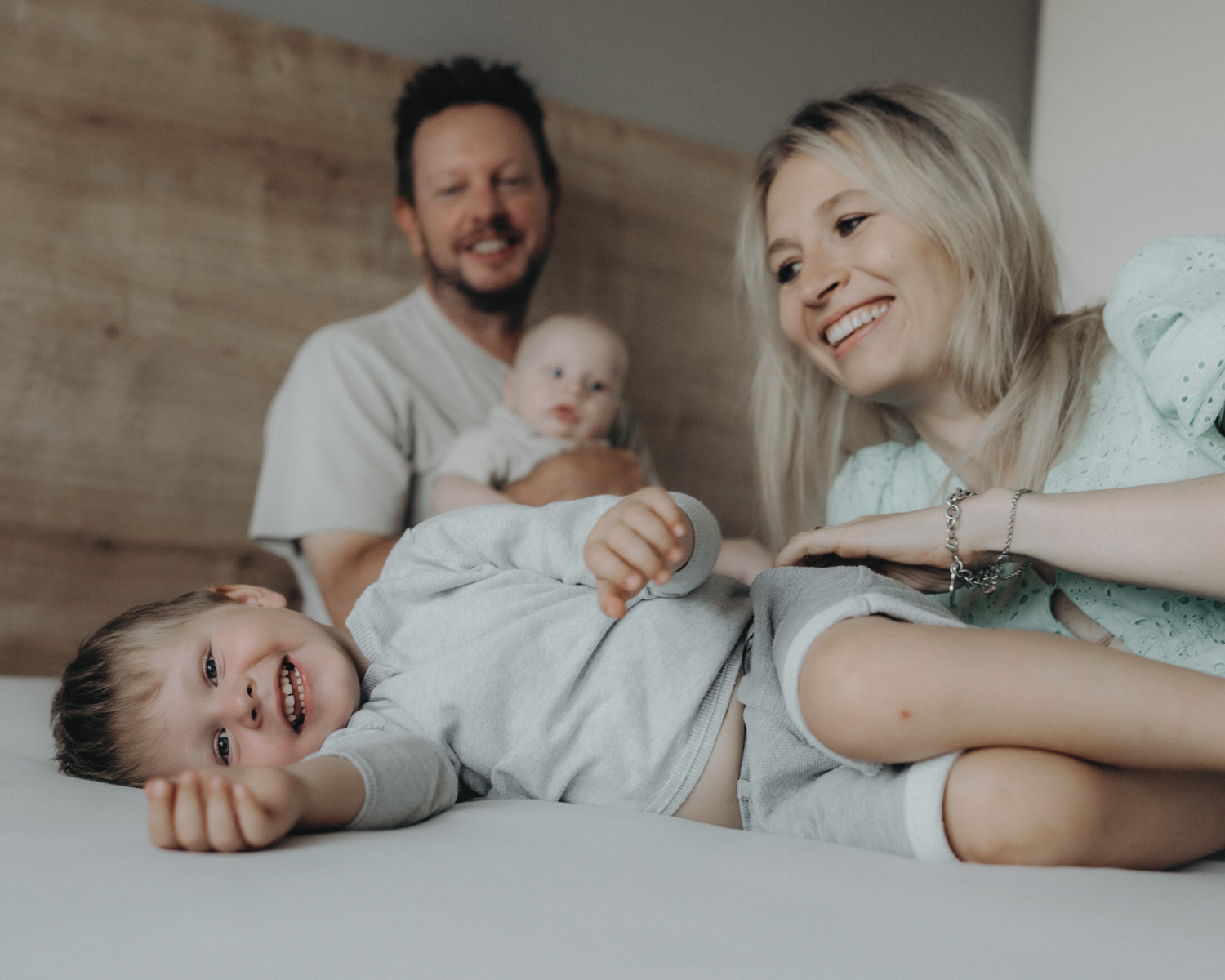 The two founders, Matt and Magda, smiling with their two children, a toddler and an infant, as they enjoy quality family time together on a bed, embodying SnuggleBox's mission.