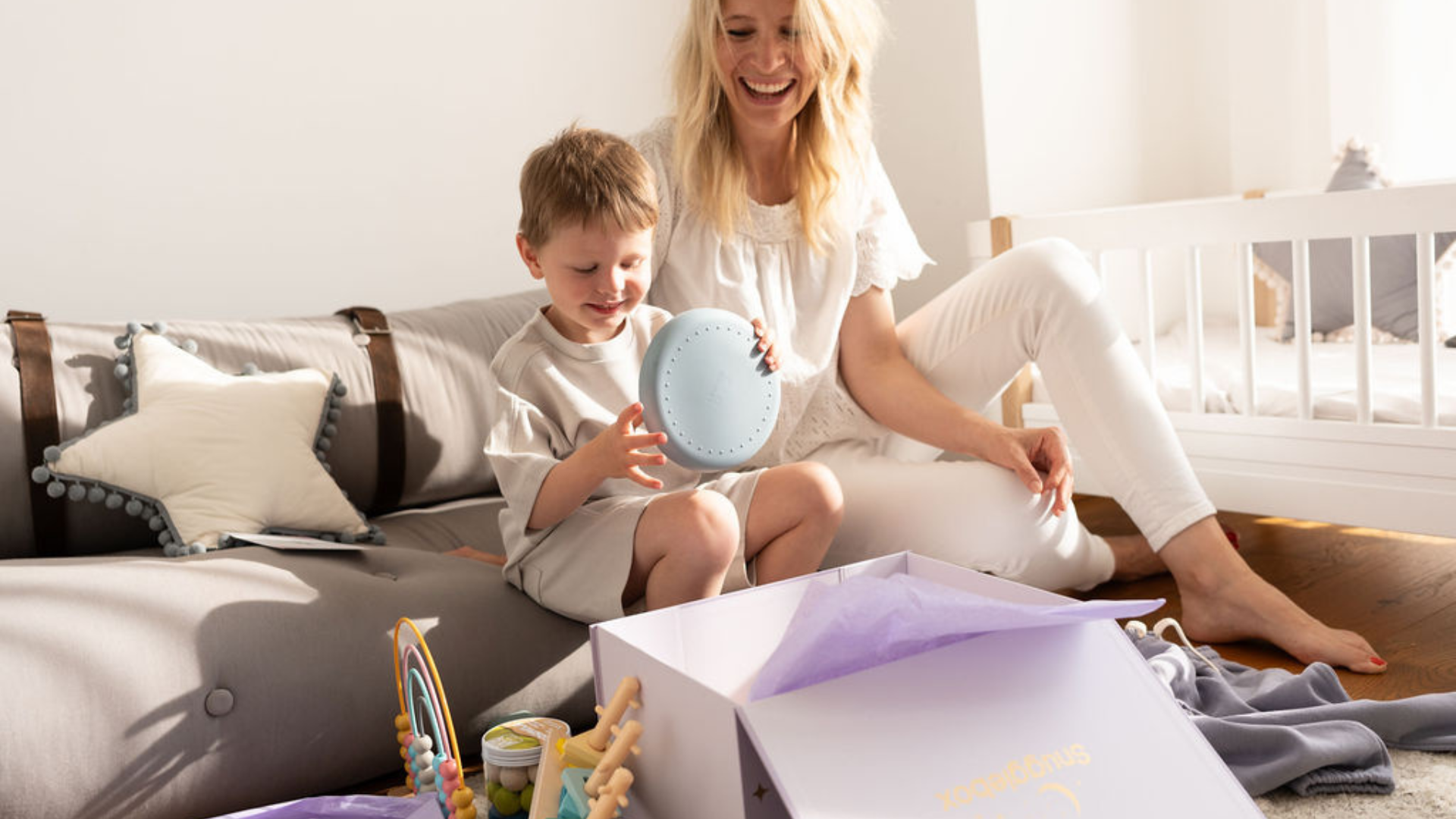 Load video: Happy mother and child unboxing a Snugglebox, revealing exciting new toys and clothing for kids.